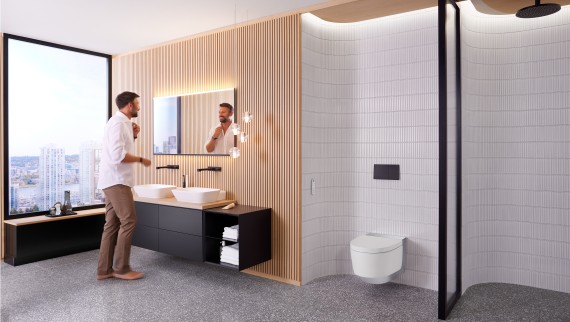 Mann på badet som står foran Geberit Option Plus Firkantet speil og svart Geberit ONE baderomsmøbel (© Geberit) Mann på badet som står foran Geberit Option Plus Firkantet speil og svart Geberit ONE baderomsmøbel (© Geberit)