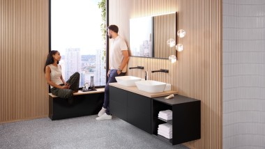 Kvinne sitter i vinduskarmen på badet med Geberit ONE-produkter og snakker med mannen Kvinne sitter i vinduskarmen på badet med Geberit ONE-produkter og snakker med mannen