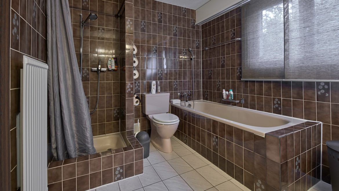 Bad med smalt dusjhjørne, badekar og gulvstående toalett